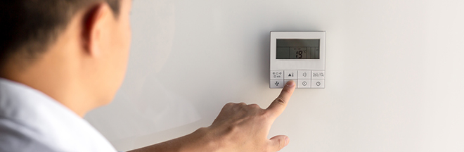 The hand of a young man in a white shirt turns on the control buttons of the air conditioner hanging on the wall