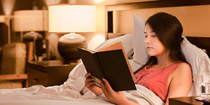 Girl reading book in bed at night with yellow lamp light on walls