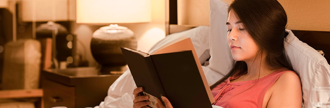 Girl reading book in bed at night with yellow lamp light on walls