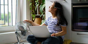 Relaxed woman typing on laptop while cooling by floor fan at home