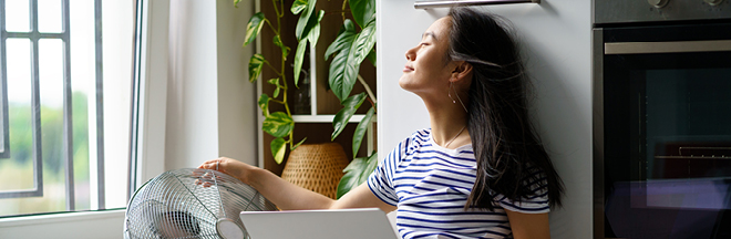 Relaxed woman typing on laptop while cooling by floor fan at home