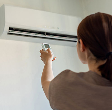 Woman adjusts an indoor heat pump unit with a remote