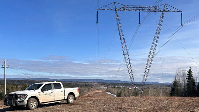 BC Hydro truck parked near a large power transmission tower in a rural landscape.