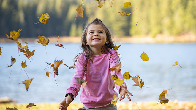 Little girl throwing leaves with a lake back drop.