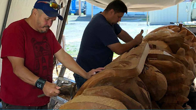 Two people carving a totem.