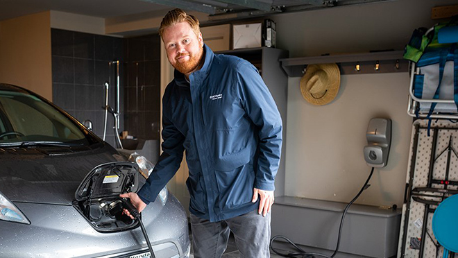 BC Hydro spokesperson Dave is standing in a garage, plugging a charger into an EV.