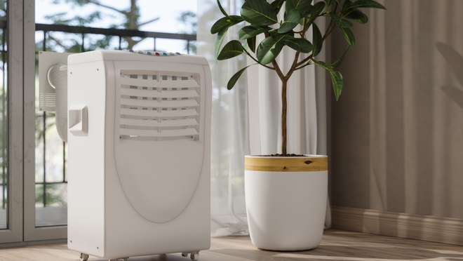 Portable air conditioning unit cooling a room, placed next to a potted plant near a large window.