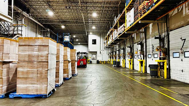 Lineage Logistics warehouse. Boxes on pallets and multiple truck garage doors are lined up in rows.