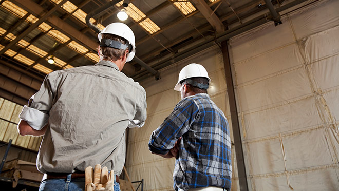 Two workers with hard hats discussing inside an industrial warehouse