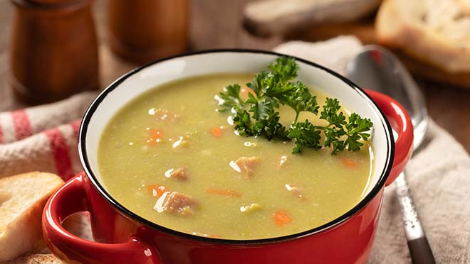 A bowl of split pea soup with a side of bread. 