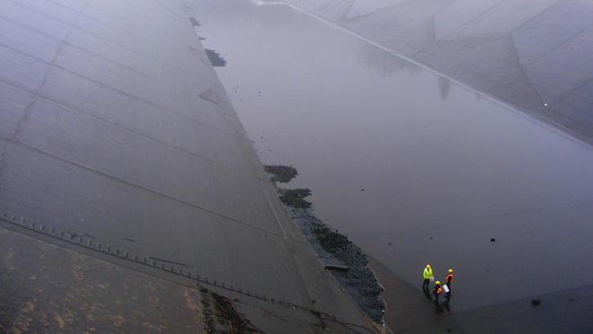 Drained section of the Kootenay Canal during maintenance work, with workers inspecting the canal bed.
