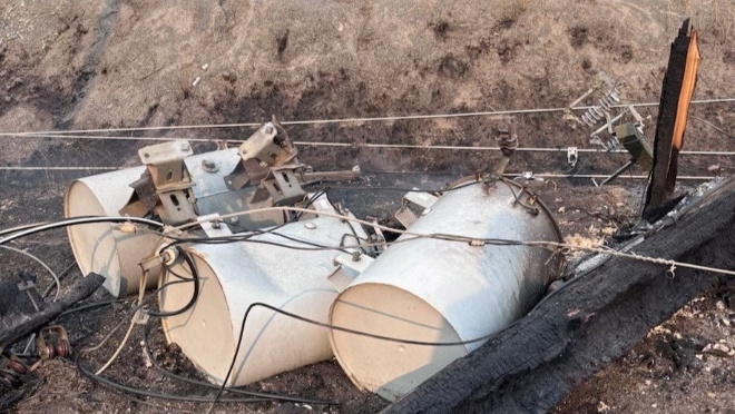 A hydro pole, transformers, and wires lying on the ground, damaged by wildfire.