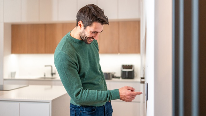 A man adjusting the thermostat in a sleek, with a modern kitchen in the background.