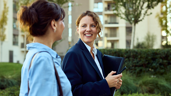 A female homeowner consults a tablet held by a technician, discussing the settings of an external heat pump unit. 