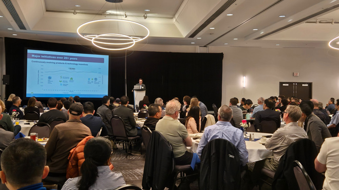 Speaker presenting at the Alliance Breakfast to an audience seated at round tables