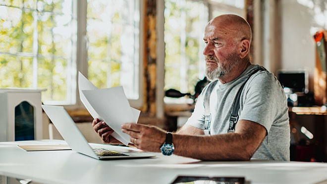 A contractor looks at documents and plans while seated at a table in a workshop