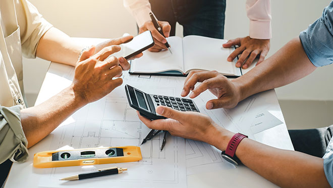 Engineers work together at an office desk to plan a construction project