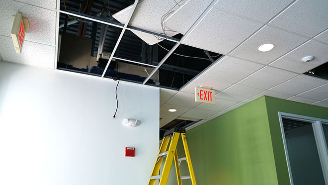 Construction site of an office renovation. Ceiling panels are being removed, with a ladder nearby.